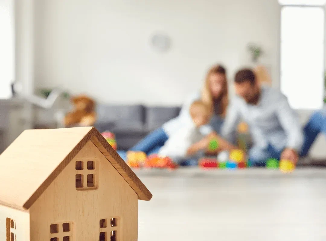 Small wodden toy house with a young family in the background